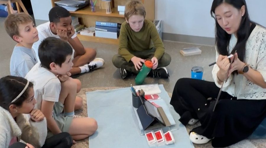 Montessori Classroom with Teacher/ Guide teaching the children in a semi circle on the floor.