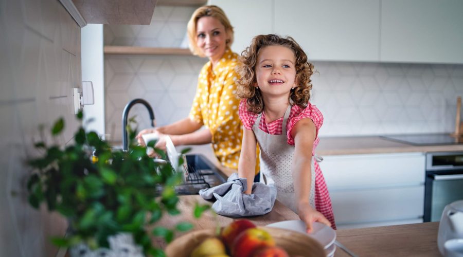 Young mother and elementary aged daughter washing dishes together.